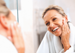 a mature blonde lady smiling in the mirror after visiting a skin clinic